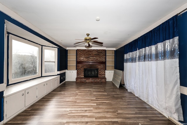 unfurnished living room featuring built in shelves, ceiling fan, wood-type flooring, and a fireplace