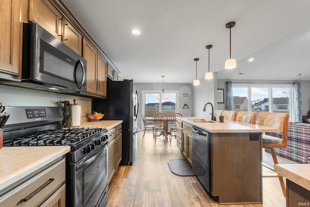 kitchen featuring sink, light wood-type flooring, appliances with stainless steel finishes, pendant lighting, and a kitchen island with sink