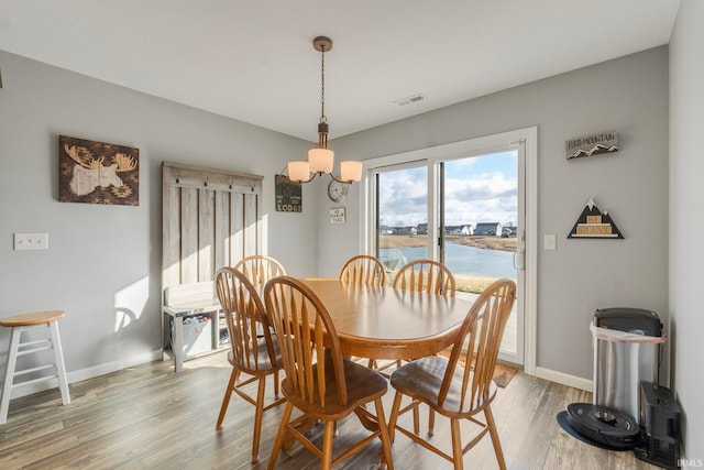 dining space with a water view, an inviting chandelier, and light wood-type flooring