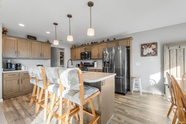 kitchen with a breakfast bar area, decorative light fixtures, appliances with stainless steel finishes, an island with sink, and light hardwood / wood-style floors