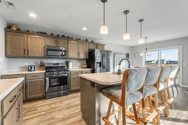 kitchen with pendant lighting, stainless steel appliances, a kitchen bar, and an island with sink