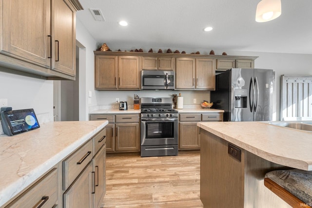 kitchen with appliances with stainless steel finishes, a kitchen bar, and light hardwood / wood-style flooring