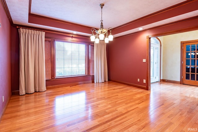 spare room featuring an inviting chandelier, ornamental molding, a tray ceiling, a textured ceiling, and light hardwood / wood-style flooring