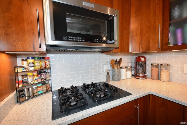 kitchen with light stone counters, black gas stovetop, and backsplash