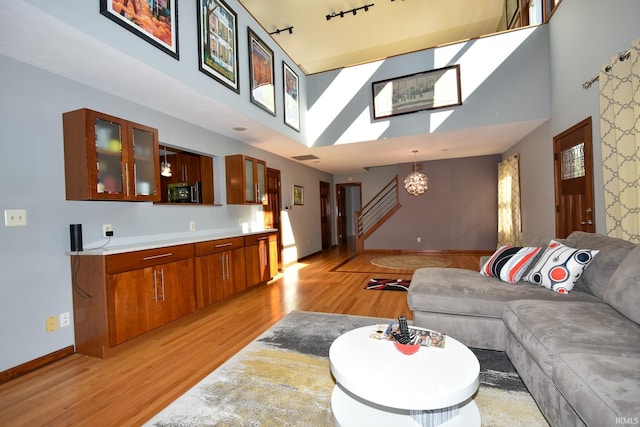 living room featuring a high ceiling, rail lighting, an inviting chandelier, and light wood-type flooring