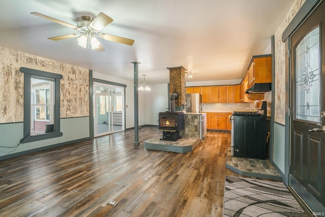 kitchen with ceiling fan, appliances with stainless steel finishes, dark hardwood / wood-style flooring, and a wood stove