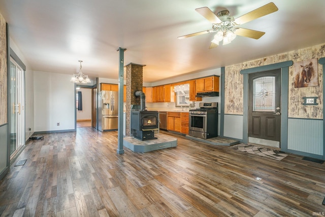 kitchen featuring appliances with stainless steel finishes, a wood stove, ceiling fan with notable chandelier, and dark hardwood / wood-style flooring