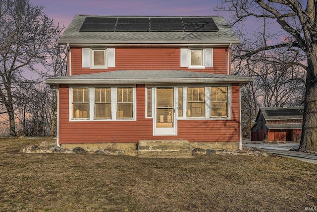 back house at dusk featuring a lawn and solar panels