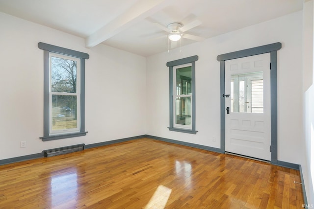 empty room featuring beamed ceiling, wood-type flooring, and plenty of natural light