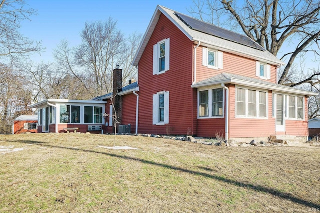 view of side of home with a yard, central air condition unit, a sunroom, and solar panels