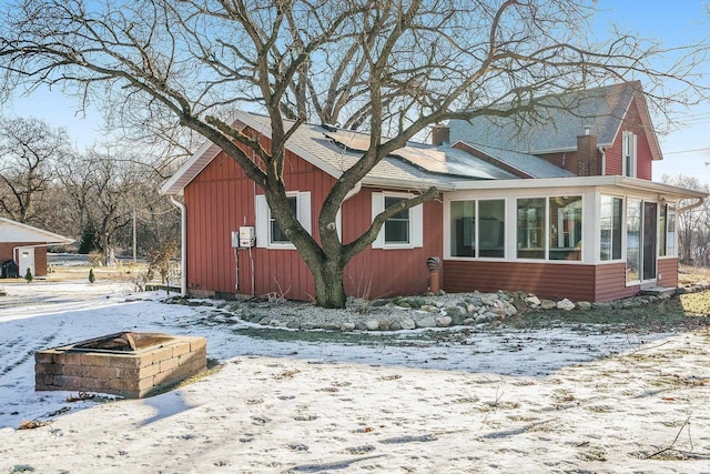 view of snowy exterior with a sunroom and an outdoor fire pit