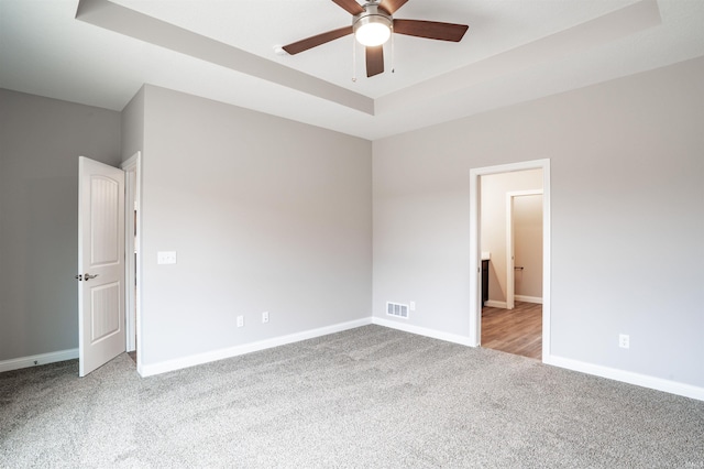 carpeted empty room with a tray ceiling and ceiling fan