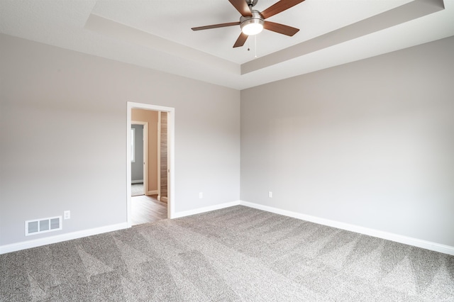 unfurnished room featuring a raised ceiling, light carpet, and ceiling fan