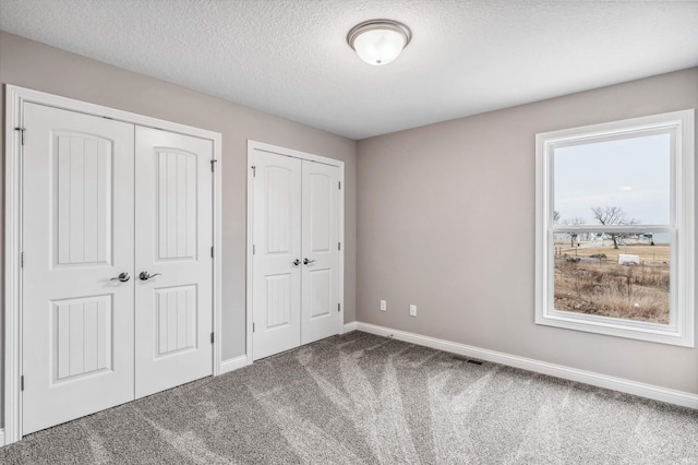 unfurnished bedroom featuring multiple closets, carpet, and a textured ceiling