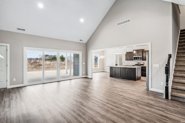 unfurnished living room with hardwood / wood-style flooring, sink, and high vaulted ceiling