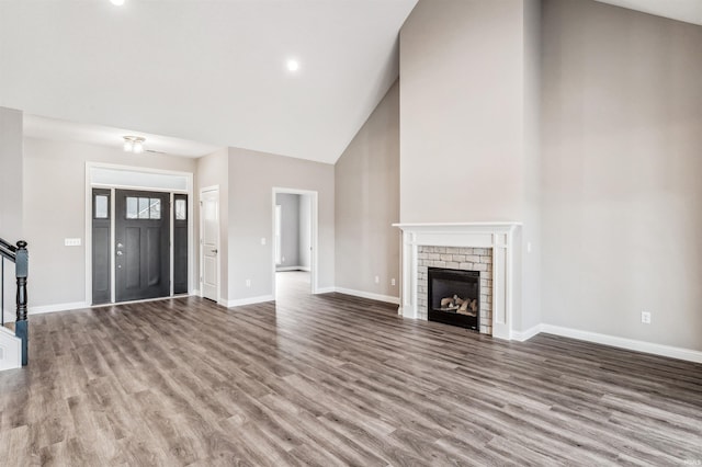 unfurnished living room with wood-type flooring, high vaulted ceiling, and a brick fireplace