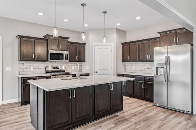 kitchen with hanging light fixtures, appliances with stainless steel finishes, sink, and a kitchen island with sink