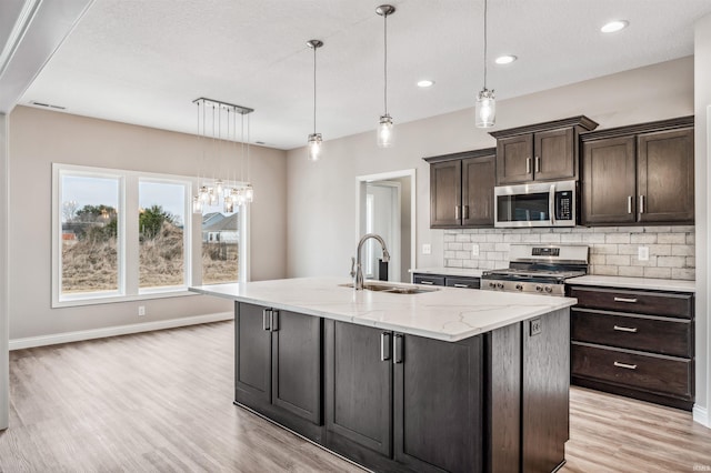 kitchen with a kitchen island with sink, sink, stainless steel appliances, and hanging light fixtures