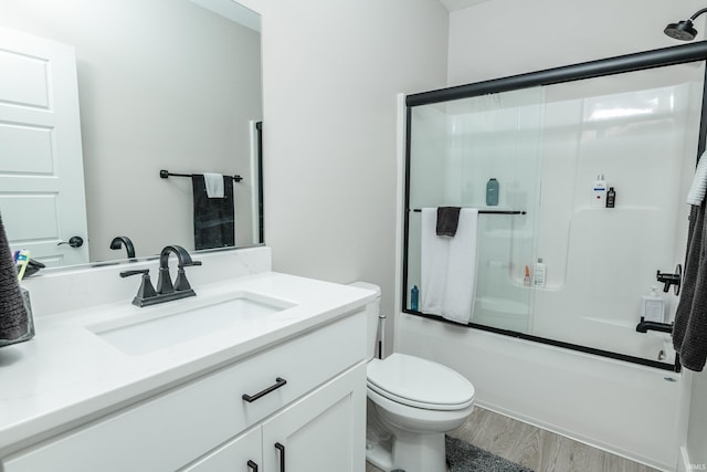 full bathroom with hardwood / wood-style flooring, enclosed tub / shower combo, vanity, and toilet