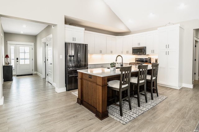 kitchen with a breakfast bar, appliances with stainless steel finishes, white cabinetry, an island with sink, and light wood-type flooring