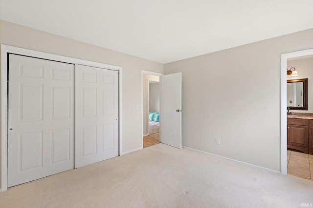 unfurnished bedroom featuring sink, ensuite bath, light colored carpet, and a closet