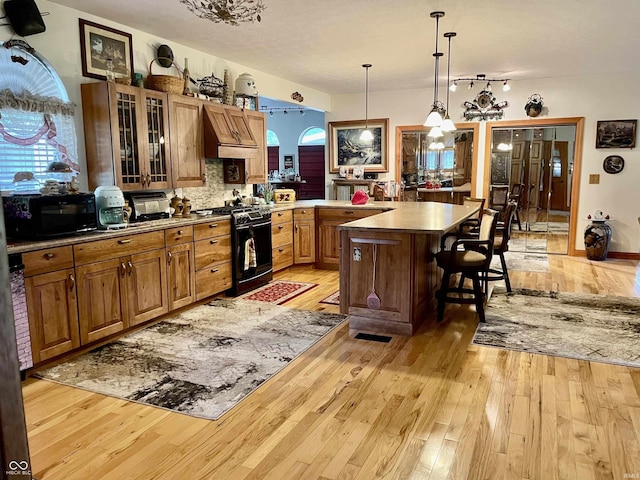 kitchen with a kitchen island, decorative light fixtures, a kitchen bar, black appliances, and light wood-type flooring