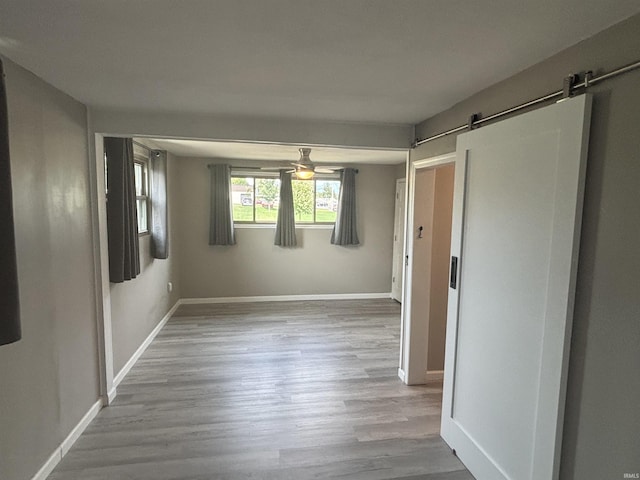 empty room with ceiling fan, a barn door, and light hardwood / wood-style floors