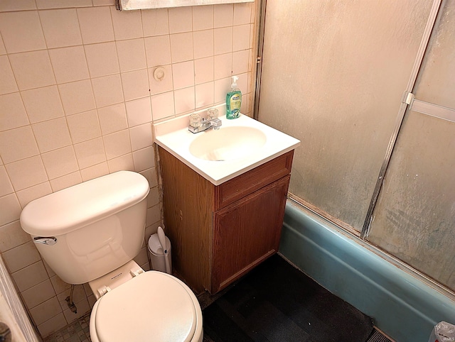 full bathroom featuring vanity, bath / shower combo with glass door, toilet, and tile walls