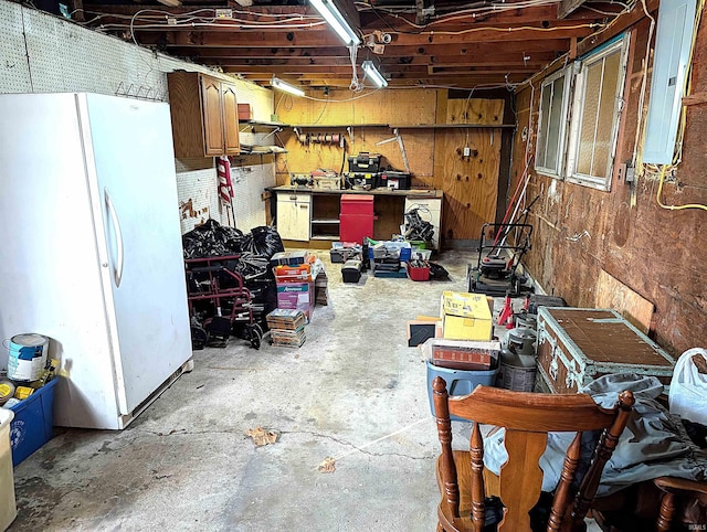 basement featuring a workshop area, electric panel, white fridge, and wood walls