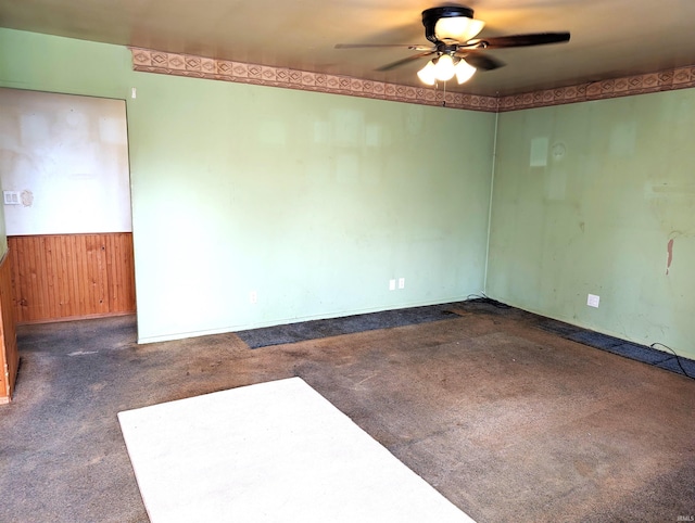 carpeted empty room with ceiling fan and wood walls