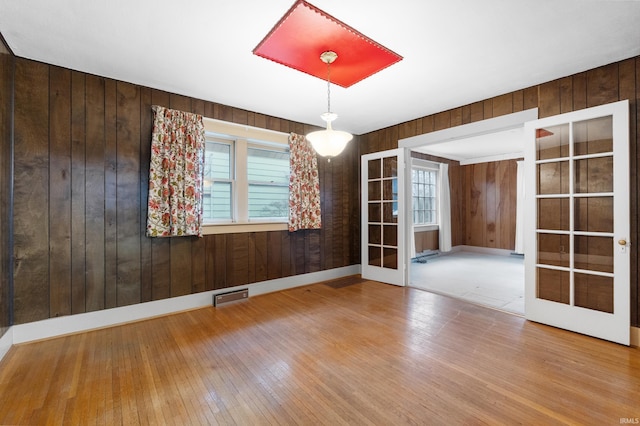 empty room with hardwood / wood-style flooring, wooden walls, and french doors