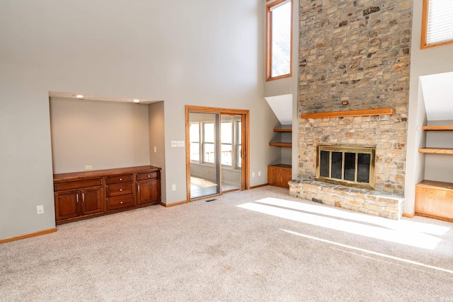 unfurnished living room with a high ceiling, a stone fireplace, and light carpet