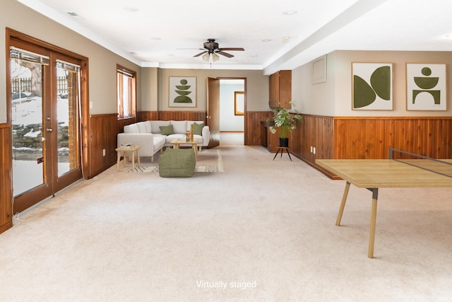 living area with ceiling fan, light colored carpet, and wood walls