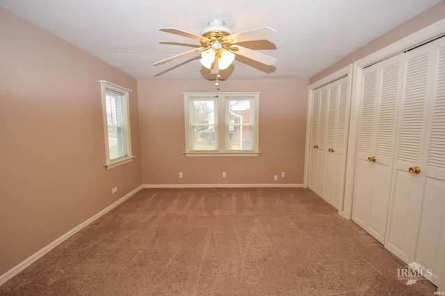 unfurnished bedroom featuring multiple closets, light colored carpet, and ceiling fan