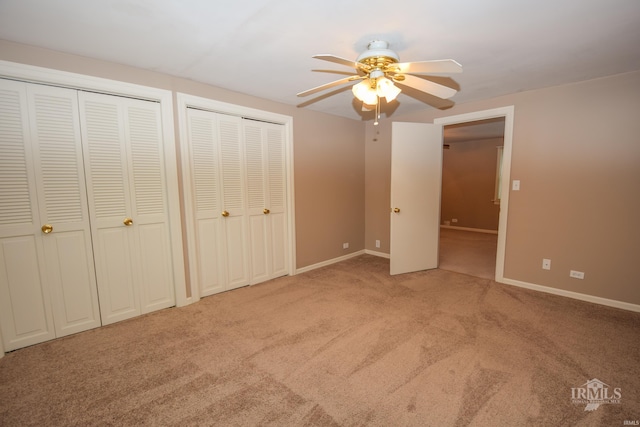 unfurnished bedroom featuring multiple closets, light colored carpet, and ceiling fan