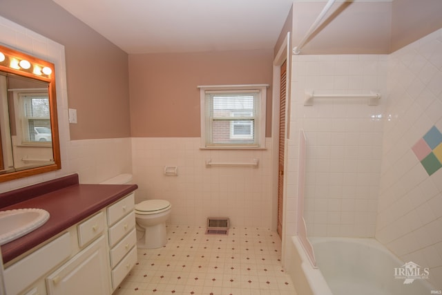 full bathroom with vanity, tiled shower / bath, tile walls, and toilet