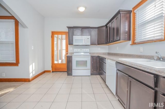 kitchen featuring sink, white appliances, light tile patterned floors, dark brown cabinets, and a wealth of natural light