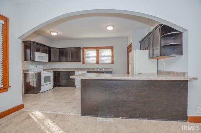 kitchen with light tile patterned flooring, sink, kitchen peninsula, dark brown cabinets, and white appliances