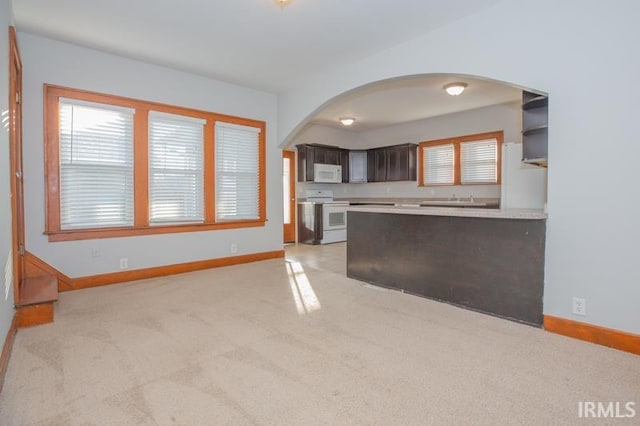 kitchen featuring dark brown cabinetry, light colored carpet, white appliances, and kitchen peninsula