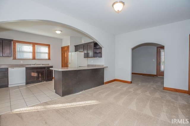 kitchen with sink, kitchen peninsula, dark brown cabinets, light carpet, and white appliances