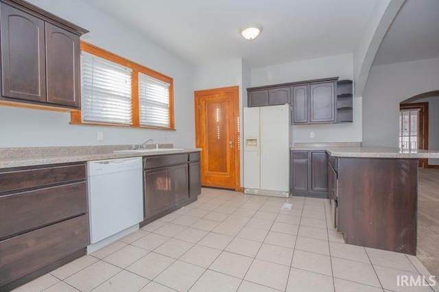 kitchen with dark brown cabinetry, light tile patterned flooring, sink, and white appliances