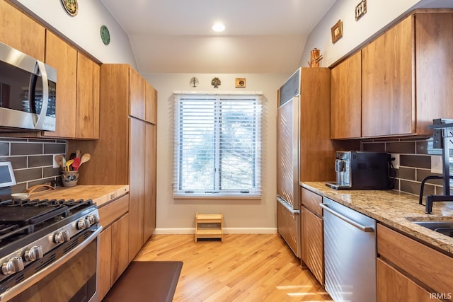 kitchen featuring light hardwood / wood-style flooring, stainless steel appliances, light stone counters, decorative backsplash, and vaulted ceiling