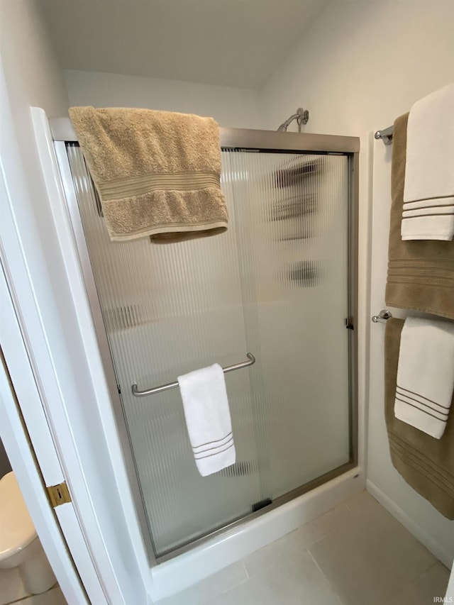 bathroom featuring a shower with door, tile patterned floors, and toilet