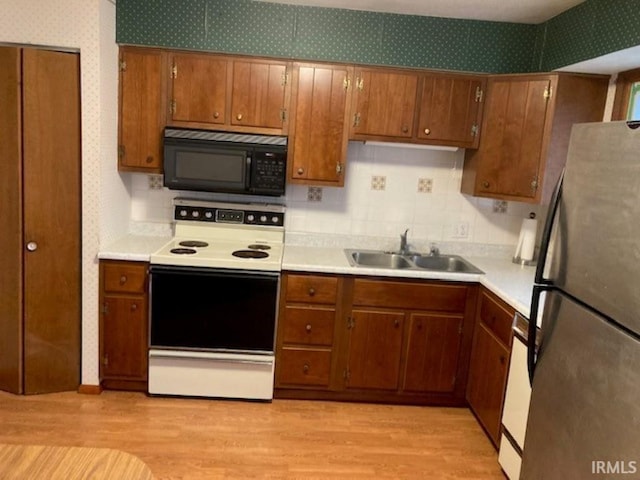 kitchen with light wood-type flooring, stainless steel fridge, sink, and white range with electric stovetop