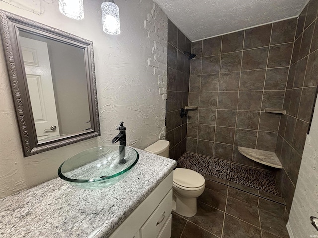 bathroom featuring vanity, a textured ceiling, toilet, and tiled shower