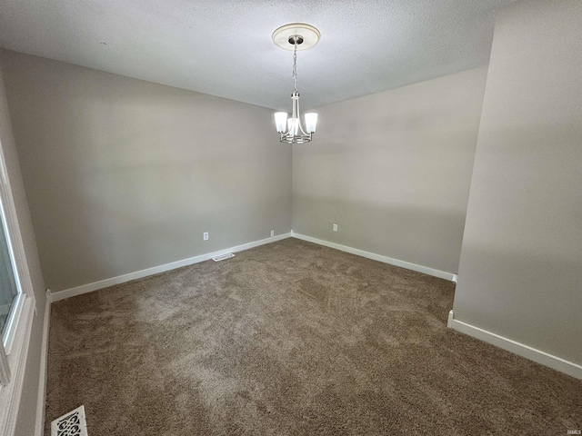 empty room with a textured ceiling, a chandelier, and dark colored carpet