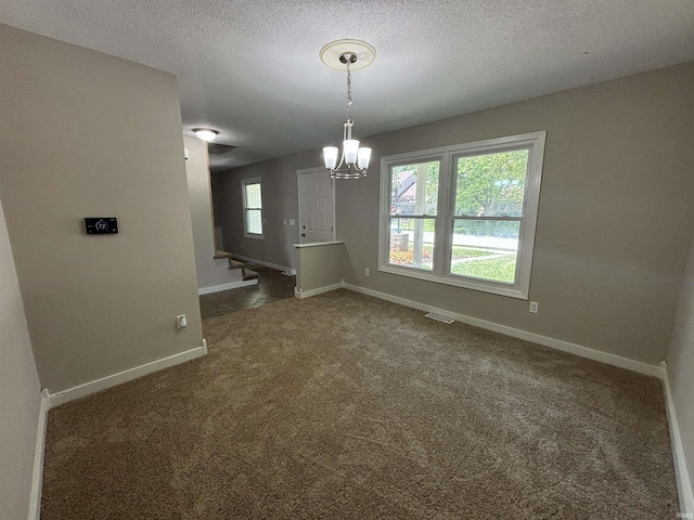 unfurnished dining area featuring a notable chandelier, a textured ceiling, and dark colored carpet