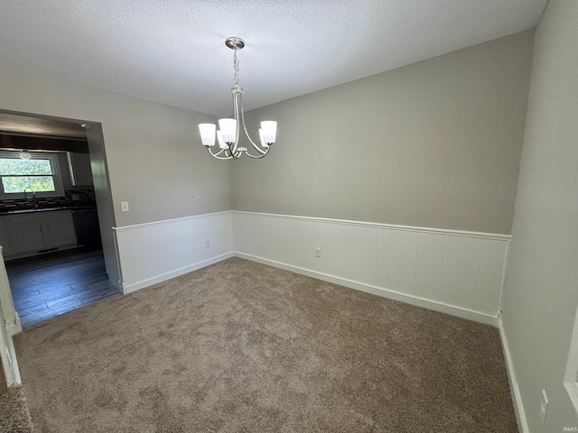 carpeted empty room featuring sink, a textured ceiling, and an inviting chandelier