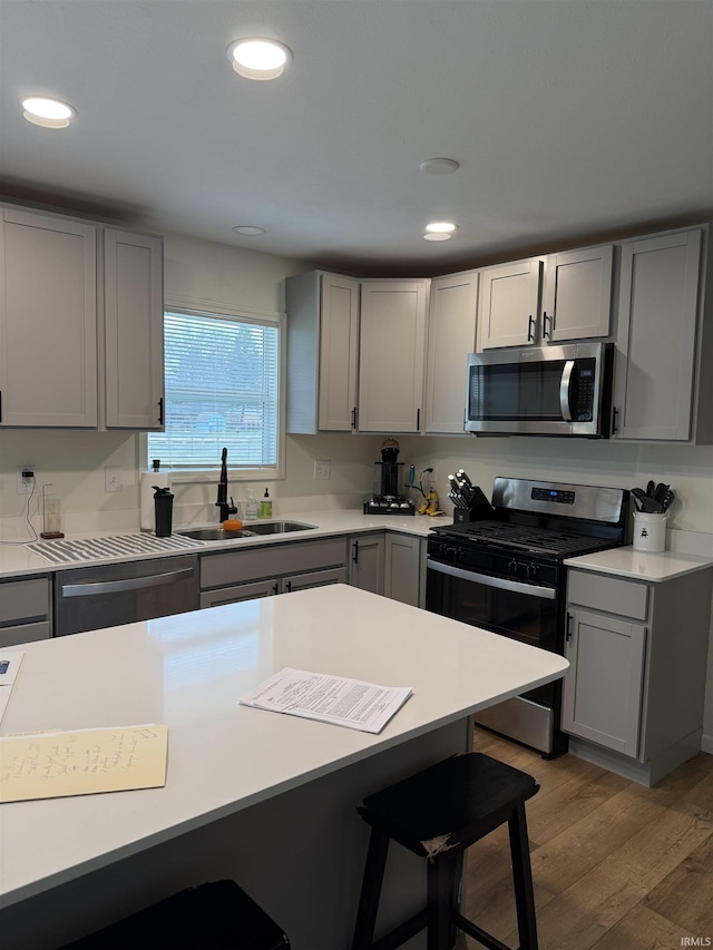 kitchen with gray cabinets, a breakfast bar, sink, stainless steel appliances, and light hardwood / wood-style flooring