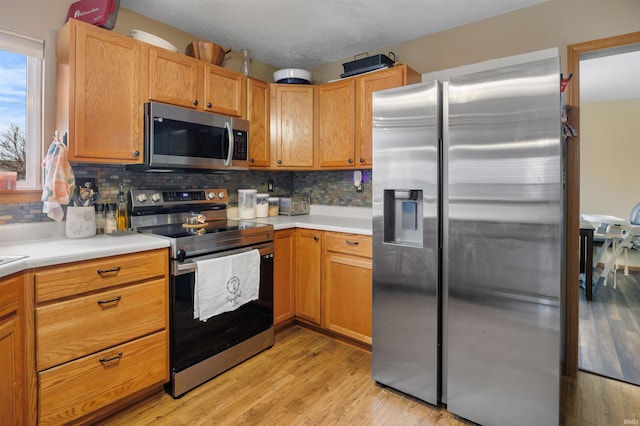 kitchen featuring appliances with stainless steel finishes, light hardwood / wood-style flooring, and decorative backsplash